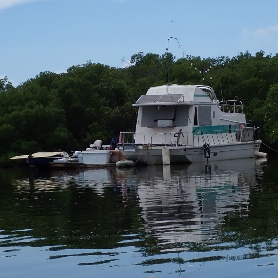 A houseboat moored against mangroves with makeshift platforms and gear attached