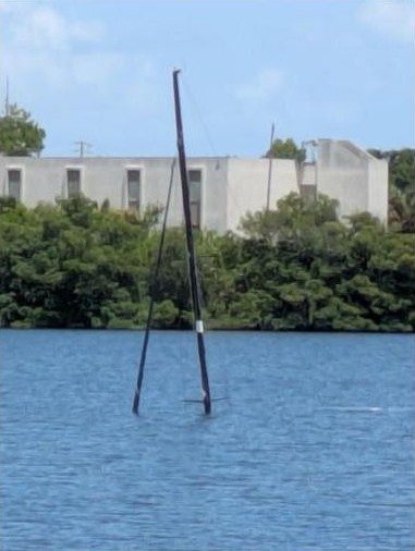 The mast of a sunken sailboat rising from the water of a Florida bay